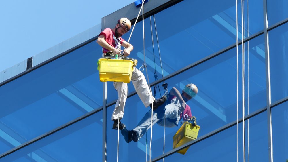 Drone window cleaning service in action – modern cleaning drone washing high-rise building glass Drone window cleaning service in action – modern cleaning drone washing high-rise building glass