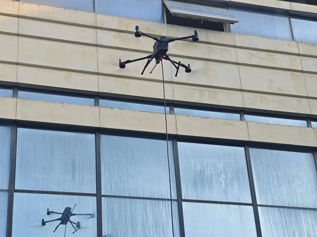 Cleaning drone spraying a high-pressure water fan along a tall glass curtain wall tower Cleaning drone spraying a high-pressure water fan along a tall glass curtain wall tower