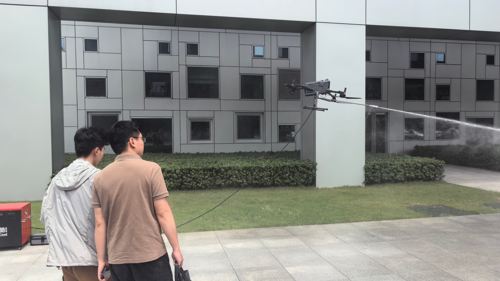 Cleaning drone spraying a high-pressure water fan along a tall glass curtain wall tower Cleaning drone spraying a high-pressure water fan along a tall glass curtain wall tower