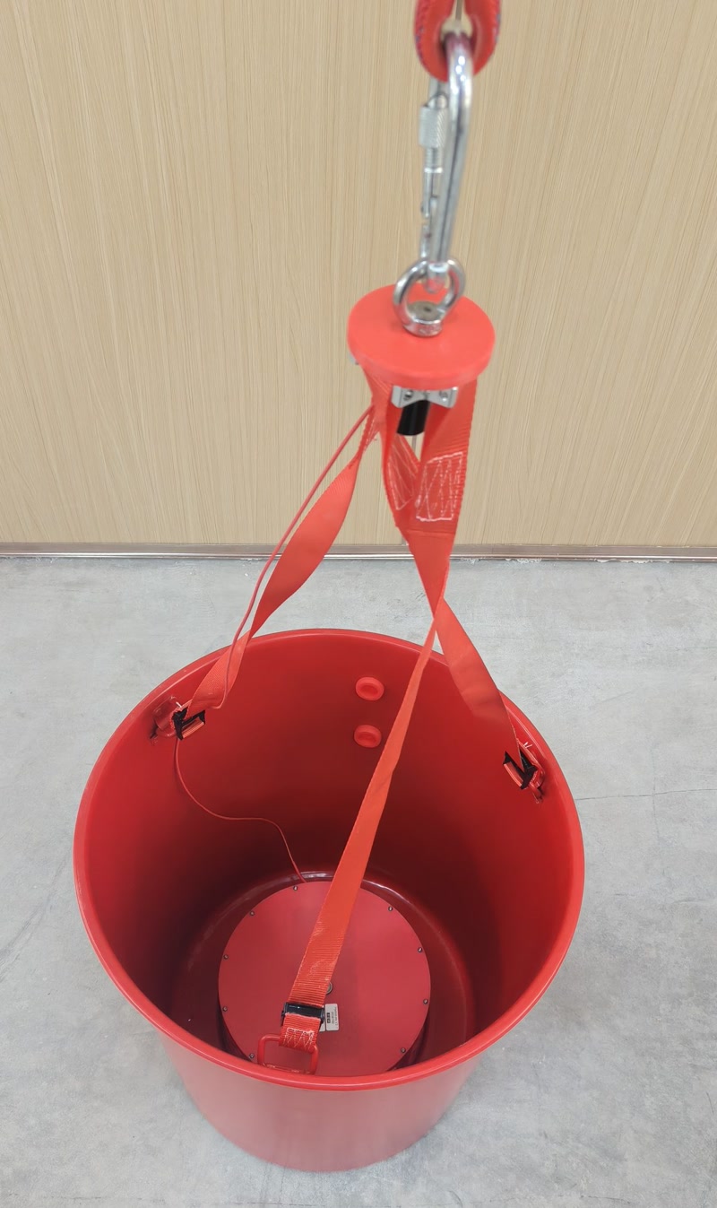 Drone carrying a red firefighting water bucket scooping water from a mountain river